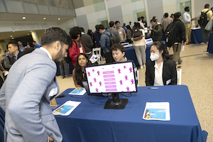 A student interacts at a table with a 3-member team participating in a CS Junior Design Capstone Expo at Georgia Tech