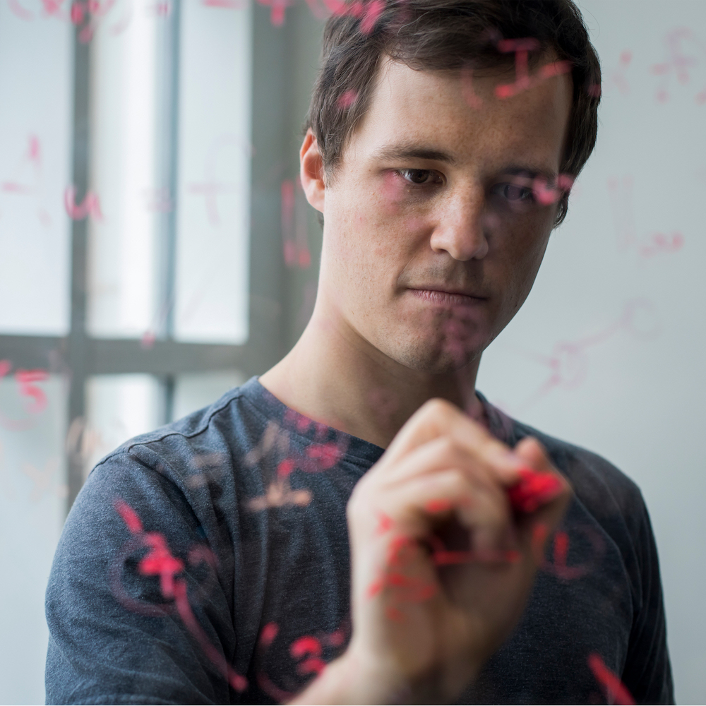 male student writing on clear board 