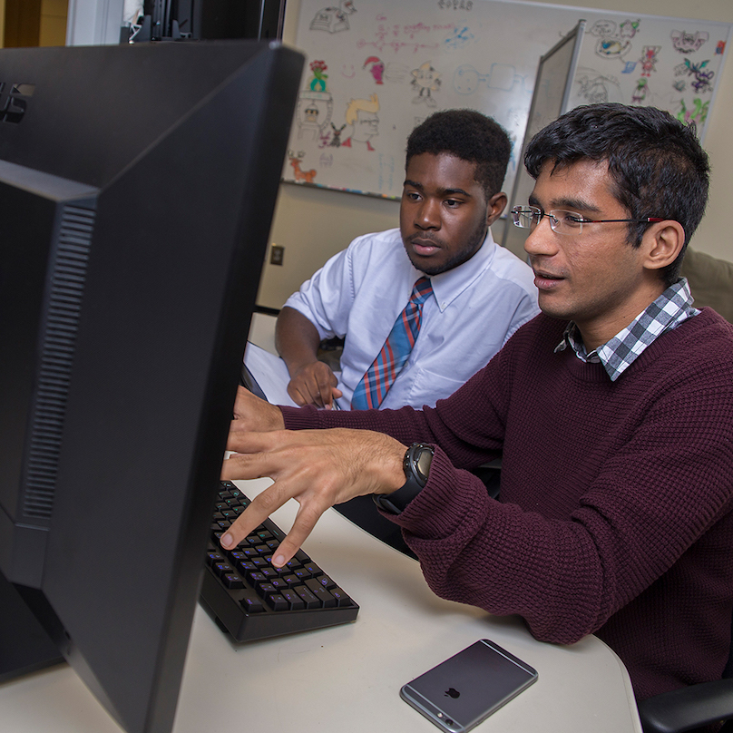 two men sit at a computer