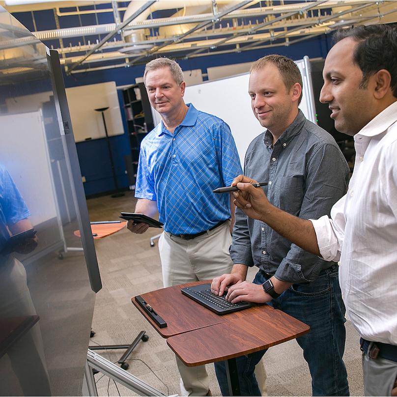 Three men gathered around a computer