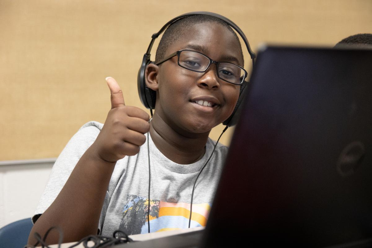 Student sitting at a computer giving a thumbs-up