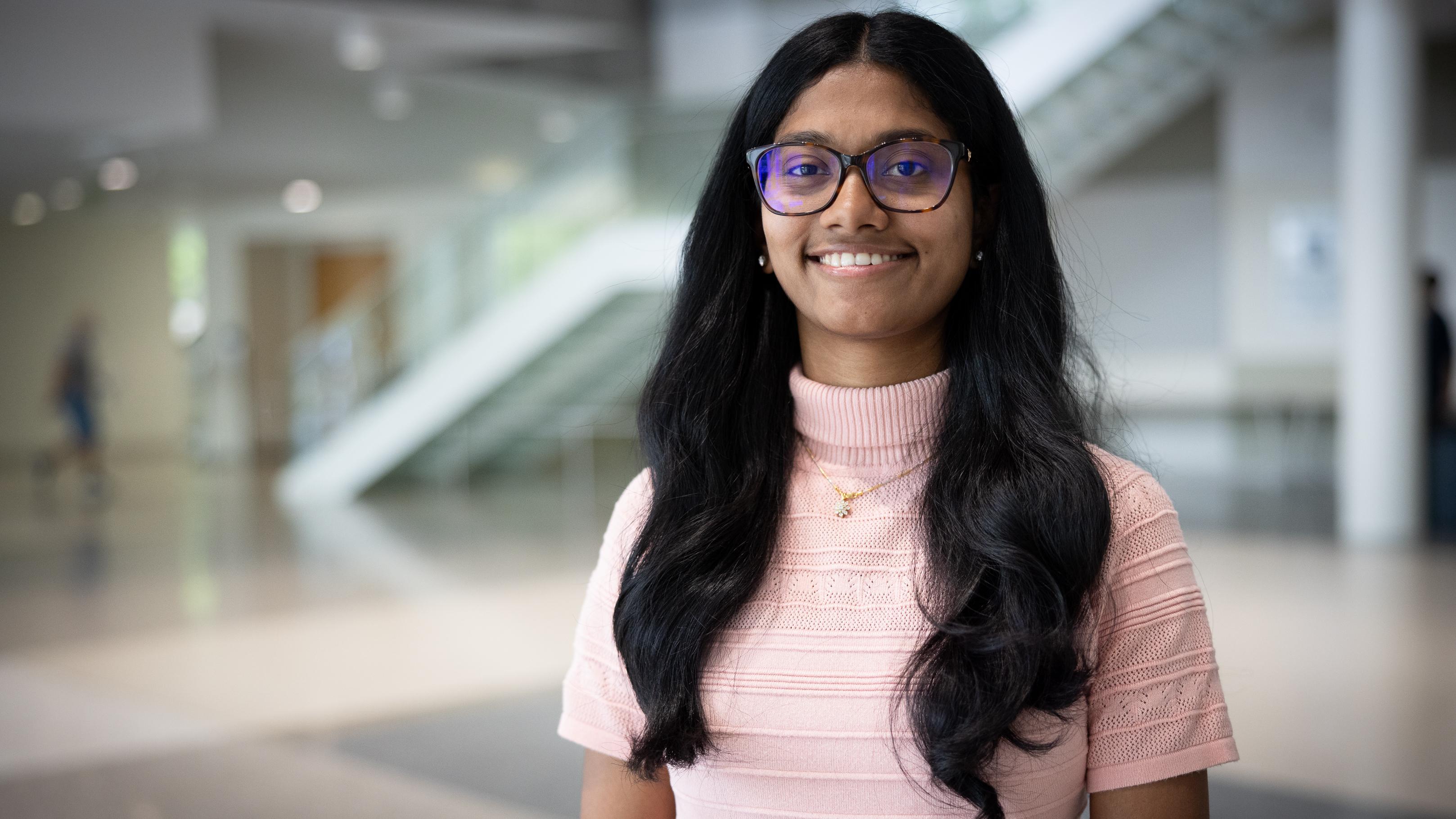 Woman wearing glasses and pink shirt stands inside smiling