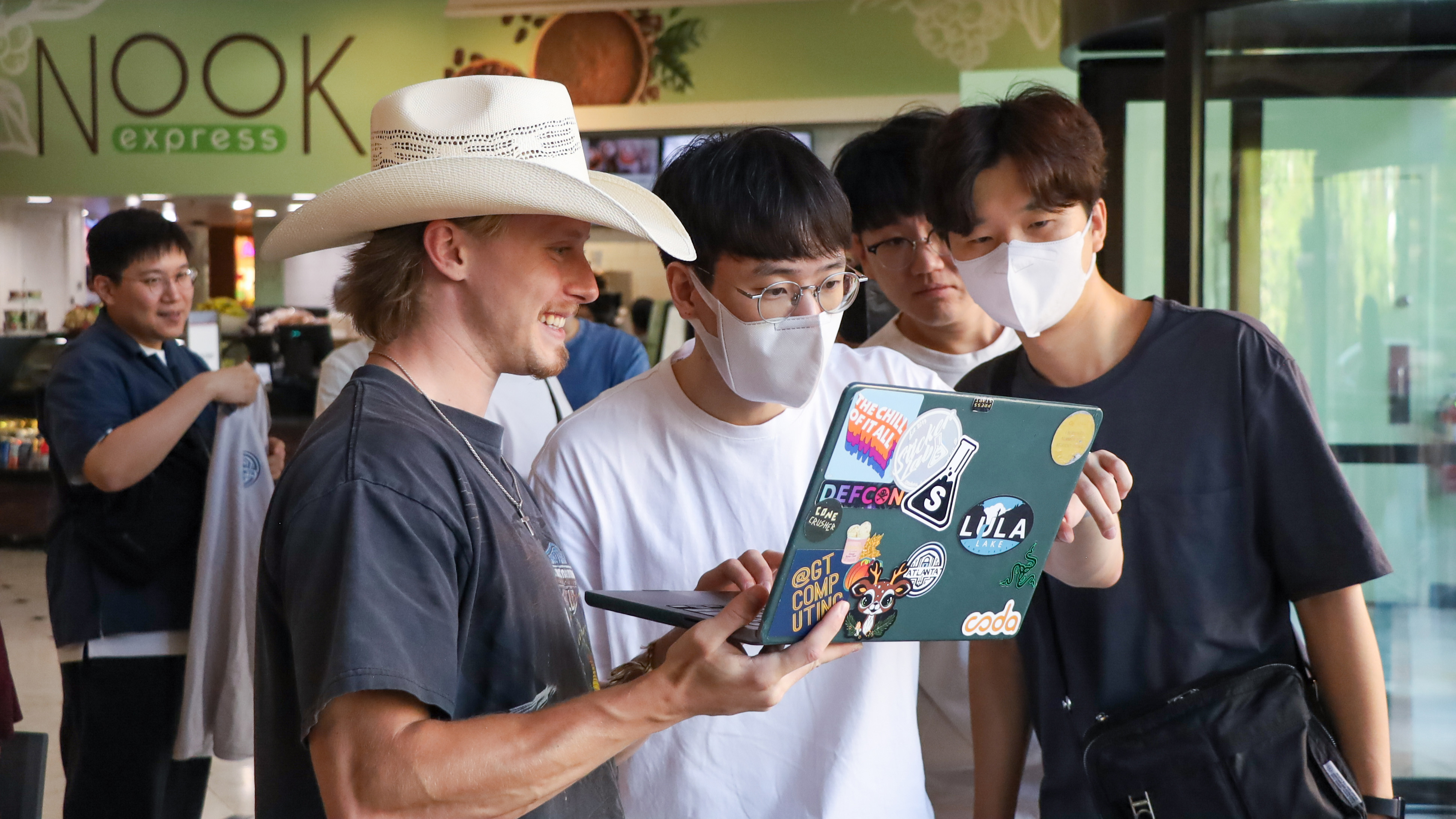 A man holds up his lapotp and lets others look on.