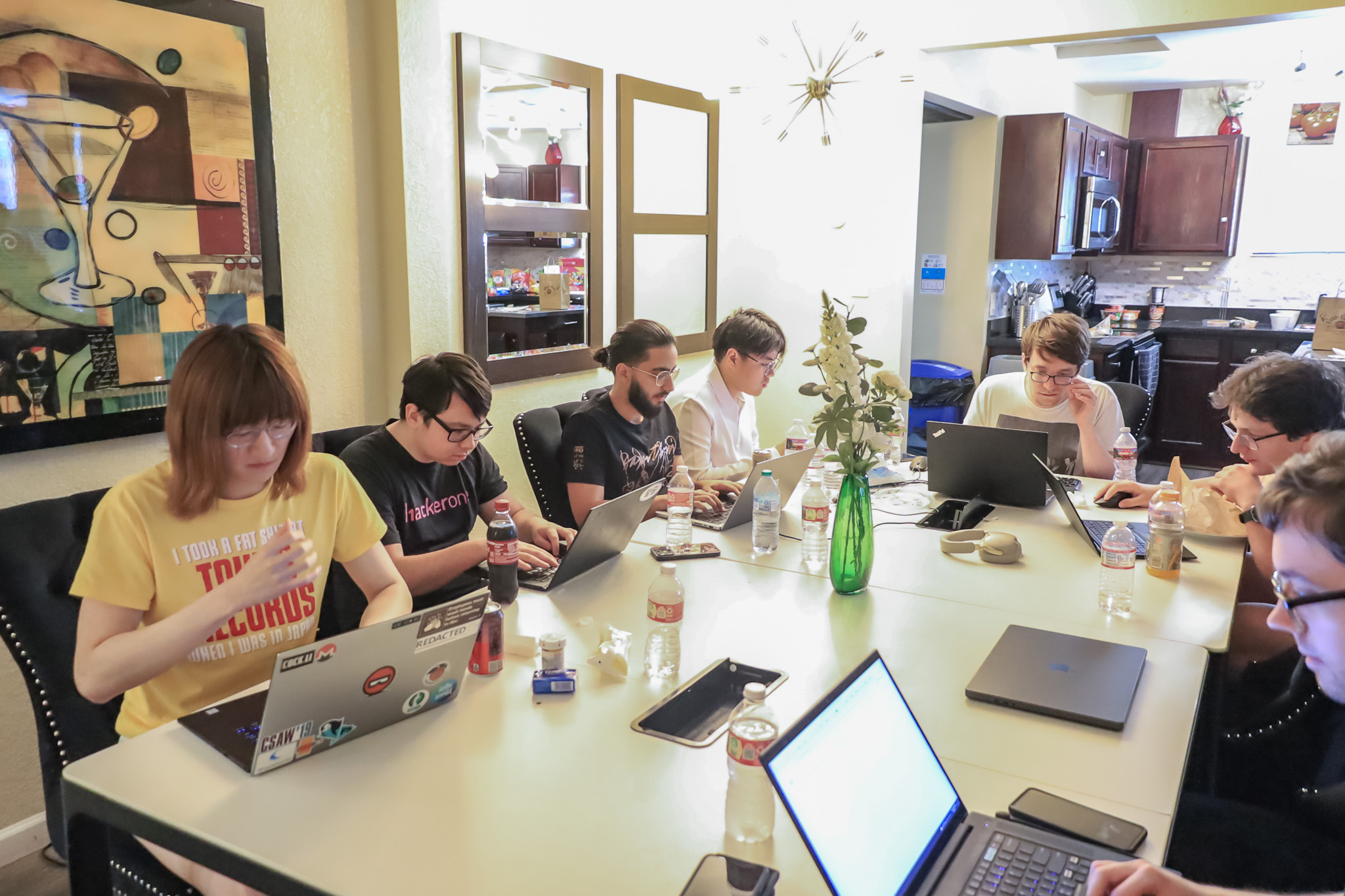 A group of people sit at a table. Each one is seated at a computer and participating in the DefCon CTF Competition