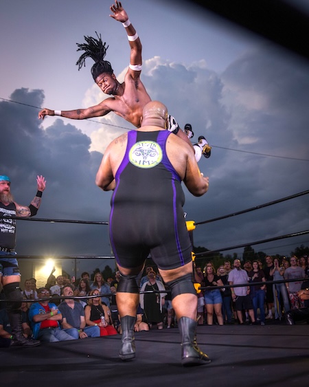 Low angle photo of indie wrestler midair after jumping off top rope toward opponent by Kevin Beasley
