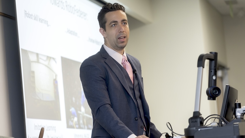 Photo of Georgia Tech's Matthew Gombolay teaching in grey three-piece suit with pink tie