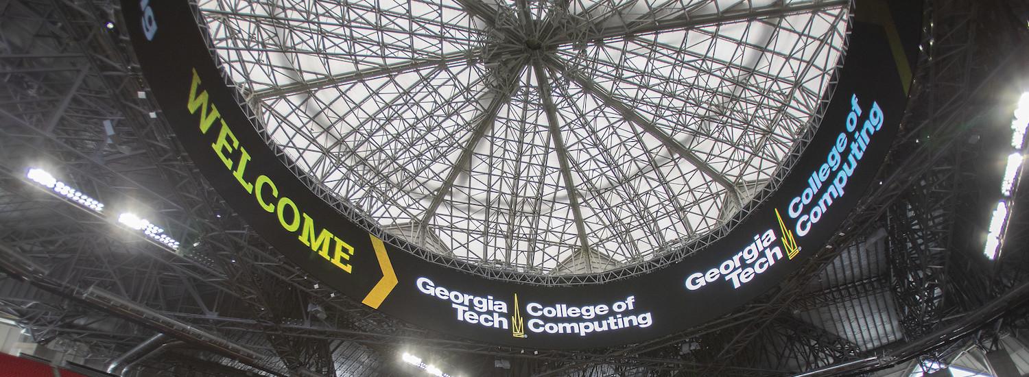 Looking up through glass ceiling at Mercedes-Benz Stadium with Georgia Tech College of Computing on marquee