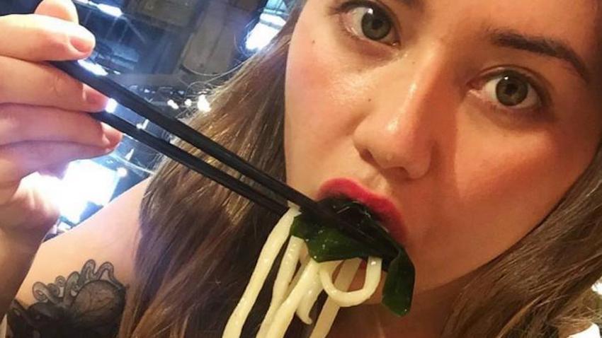 Close-up photo of a young woman eating noodles with chopsticks