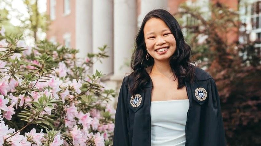 Georgia Tech Computer Science student Jillian LaTour smiling in her cap and gown with pink flowers at left and building with columns behind her