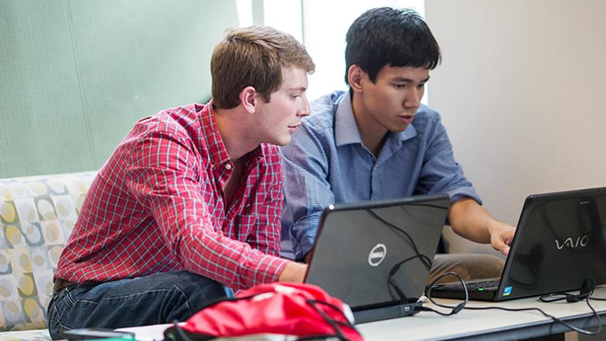 Two students sitting at desk working with one another on computer