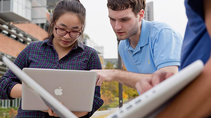 Two people look over a computer outside