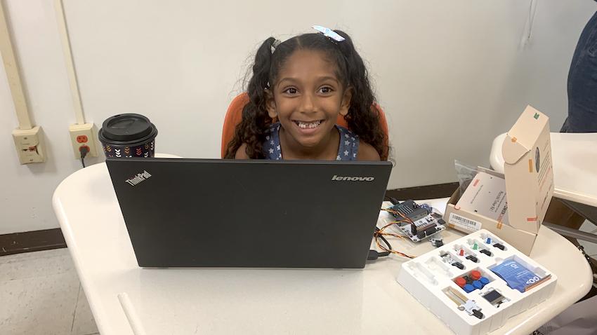 A young student from USGI smiling while working at laptop computer