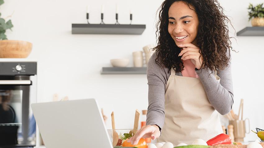 stock image of young woman cooking while following recipe from her laptop