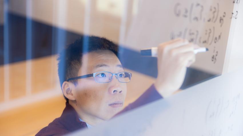 man wearing glasses writing with a marker on glass