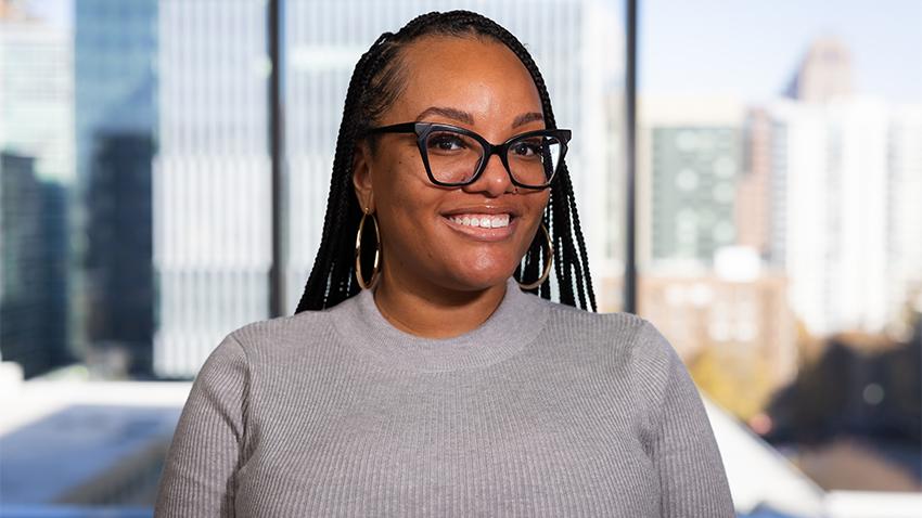 A smiling woman with braids wearing glasses and a grey sweater