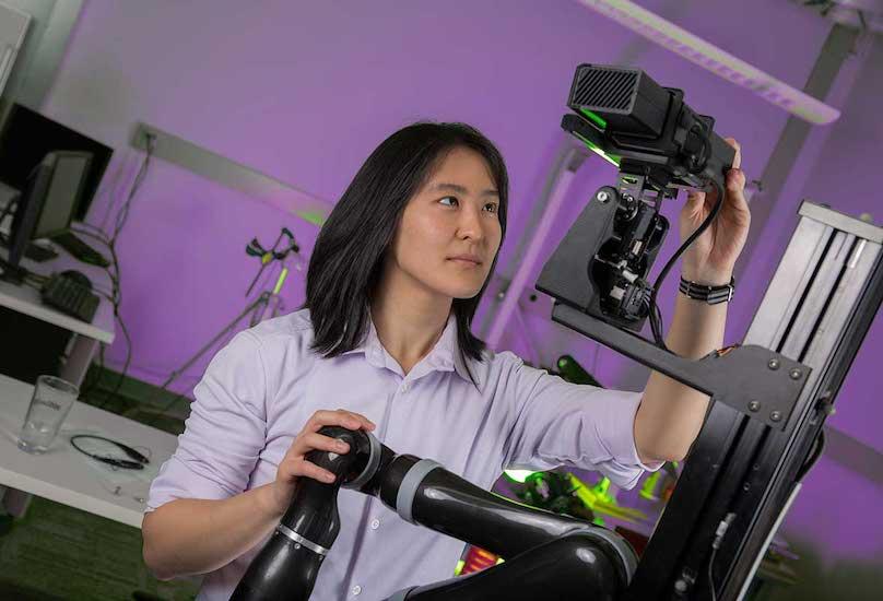 School of Interactive Computing student looks up at a robot with her hand adjusting its head.