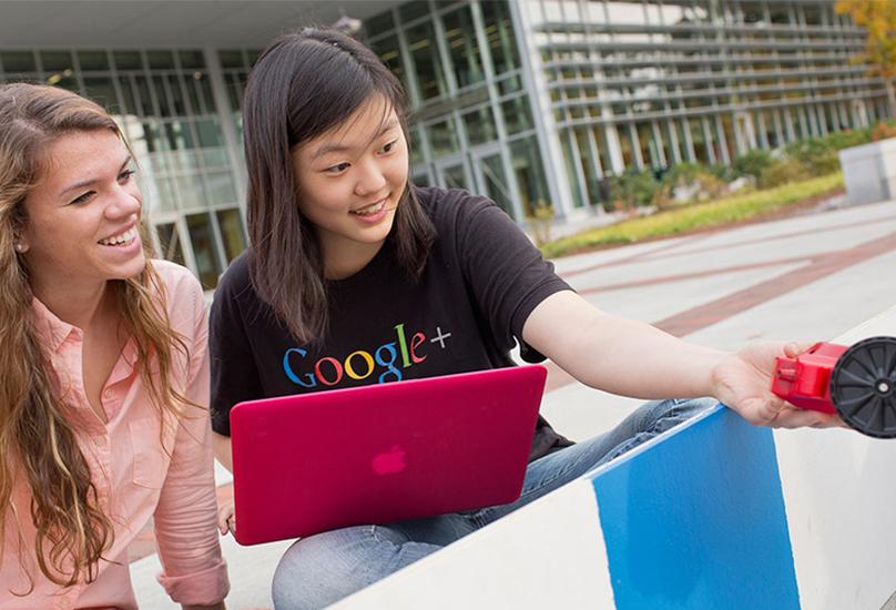 Two women sit outside with laptop and robotic toy car