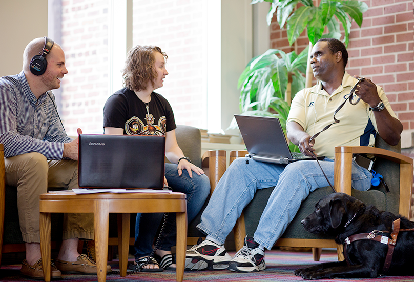 Three people conversing with laptops out in a sunny room