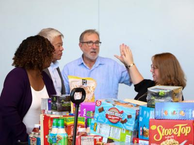 A group of people standing around a large amount of food for Klemis Kitchen. 