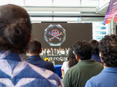 A crowd of people looking at a screen. The screen shows a team photo of Team Atlanta.