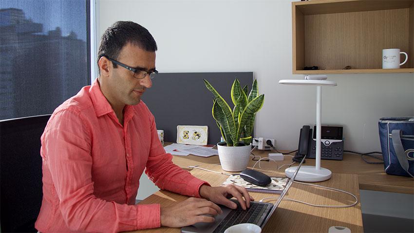 Man in salmon colored shirt sits at desk and works on computer 
