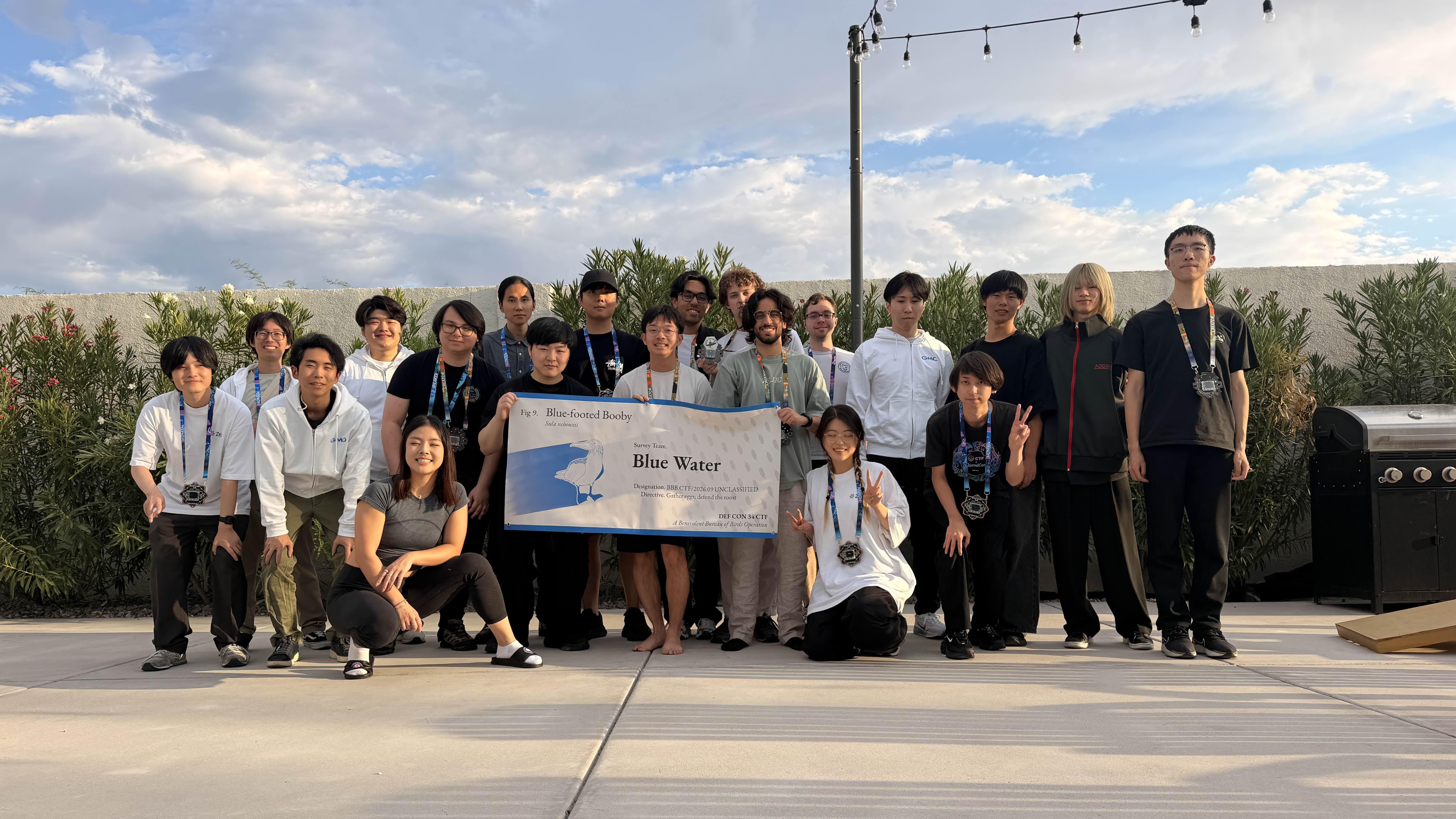 A group of people standing outside holding a banner. The banner says "Blue Water" which is the team's name.