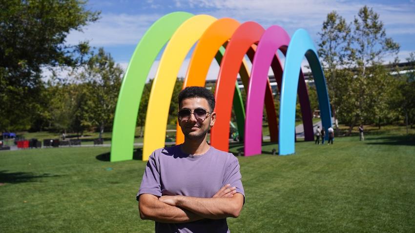 Man standing outside in front of rainbow sculpture 